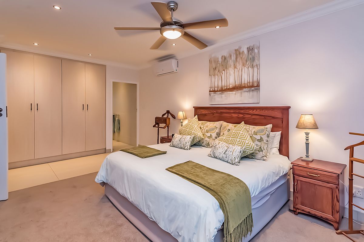 Spacious bedroom featuring built-in cupboards, carpeted flooring, a ceiling fan, and a wall-mounted split-system air conditioner.