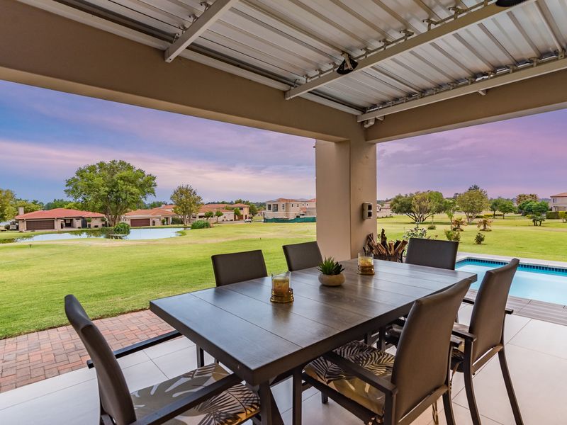 A spacious covered patio featuring tiled flooring, overlooking a private swimming pool and expansive landscaped garden views.