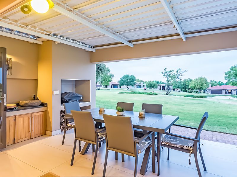 Covered patio featuring a built-in braai, stone basin, and cabinetry, overlooking a landscaped garden and golf course view.