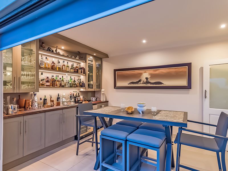 A well-appointed home bar area featuring custom built-in cabinetry, glass display shelving, an integrated wine cooler, and recessed lighting.