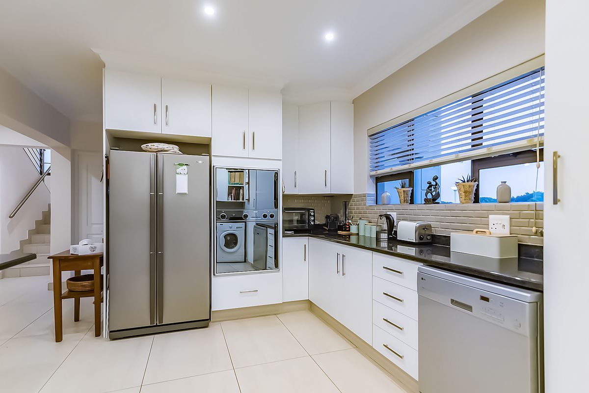 Modern kitchen featuring white cabinetry, dark stone countertops, subway tile backsplash, and integrated appliances with clean, neutral finishes.