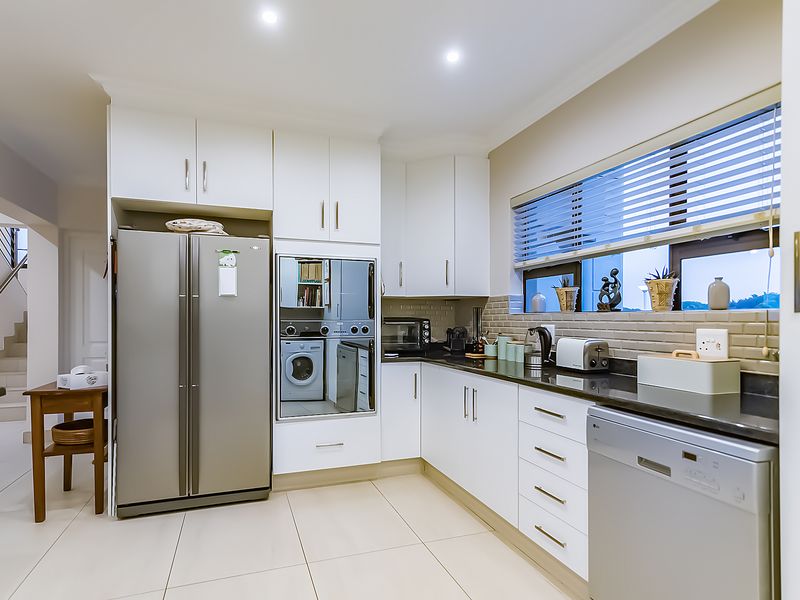 Modern kitchen featuring white cabinetry, dark stone countertops, subway tile backsplash, and integrated appliances with clean, neutral finishes.