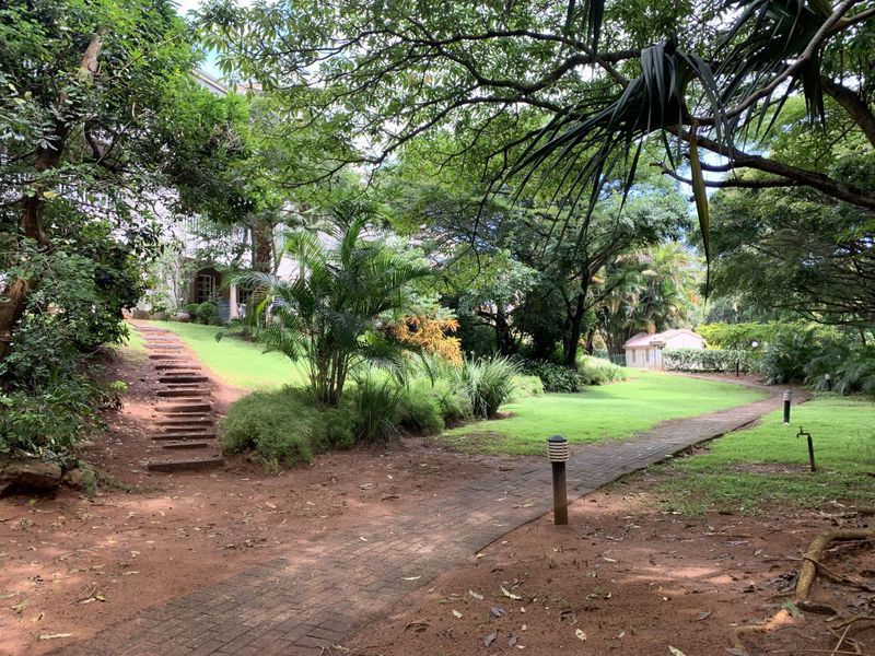 A lush, well-maintained garden area featuring a paved walkway, stone steps, and mature trees, providing a serene outdoor space.