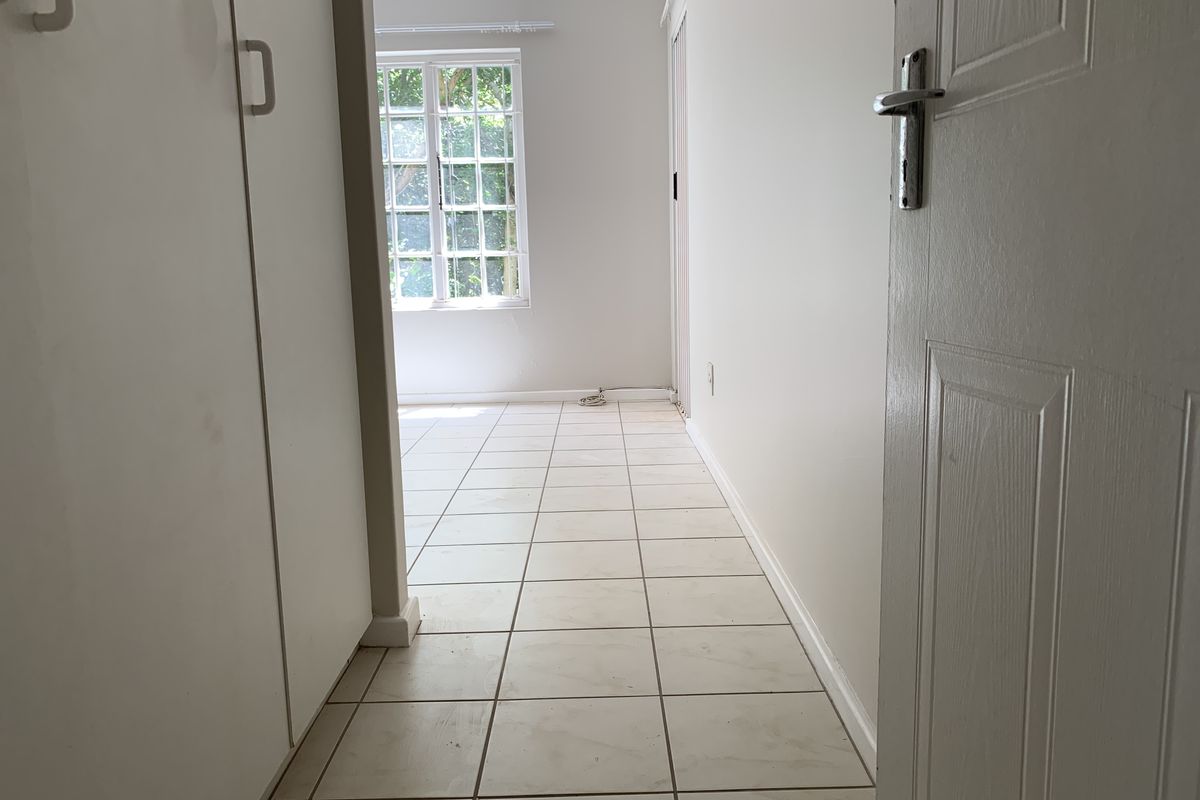 An empty bedroom featuring tiled flooring, built-in cupboards, and a window allowing natural light into the space.