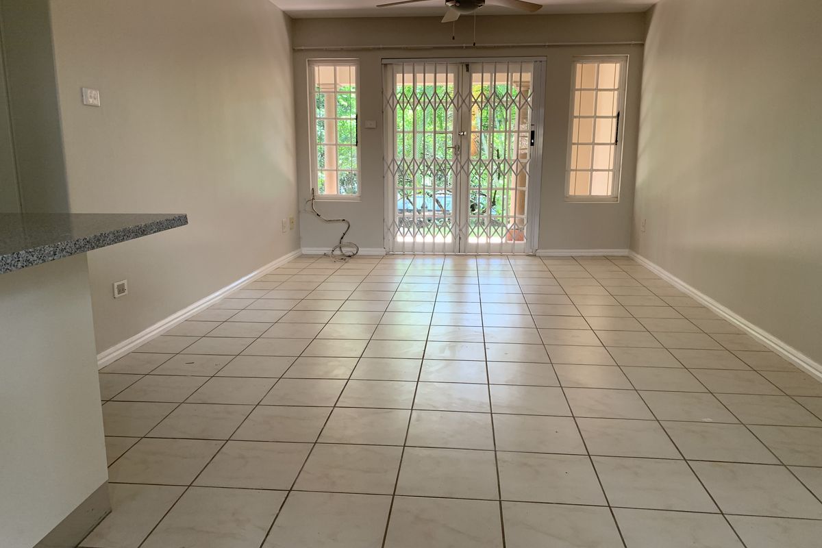 Spacious, empty living area featuring neutral tiled flooring, a ceiling fan, and sliding glass doors leading to an outdoor space.