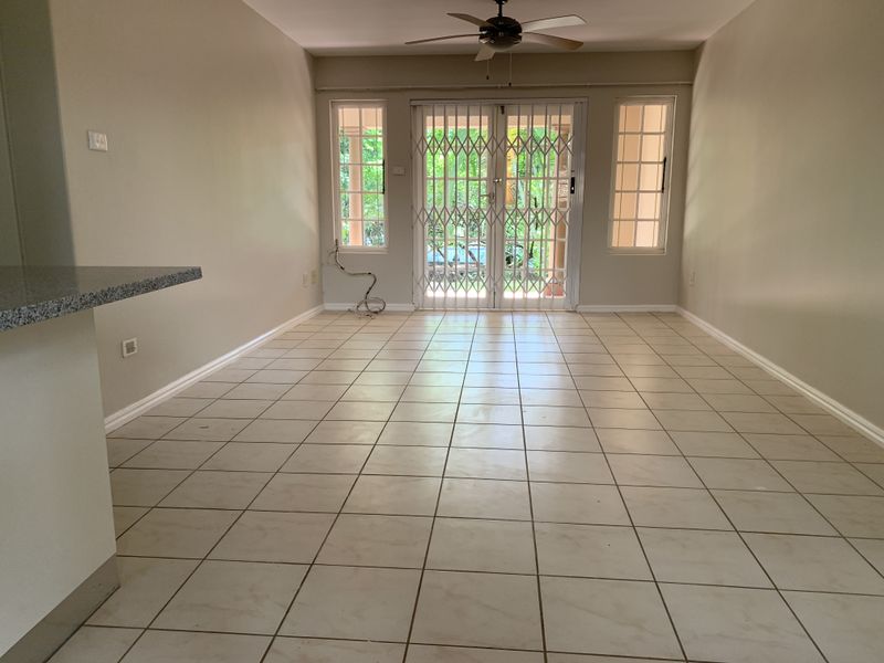 Spacious, empty living area featuring neutral tiled flooring, a ceiling fan, and sliding glass doors leading to an outdoor space.