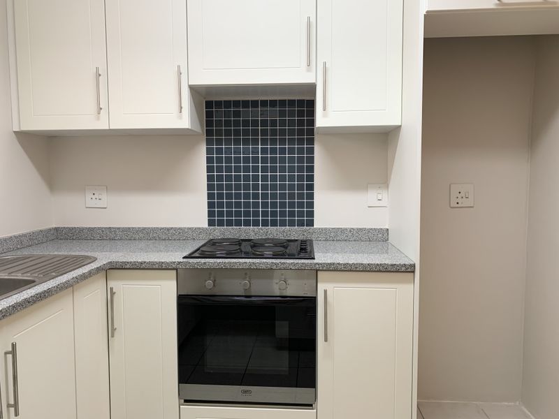 A clean, modern kitchen featuring white cabinetry, granite countertops, a tiled splashback, and integrated stainless steel oven and hob.