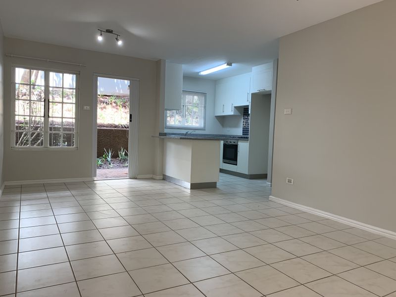 Spacious open-plan living area featuring neutral tiled flooring, a modern kitchen with built-in appliances, and direct access to an outdoor patio area.