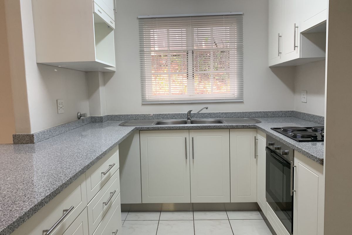 A clean, modern kitchen featuring white cabinetry, granite countertops, a built-in oven, electric hob, and a stainless steel double sink.