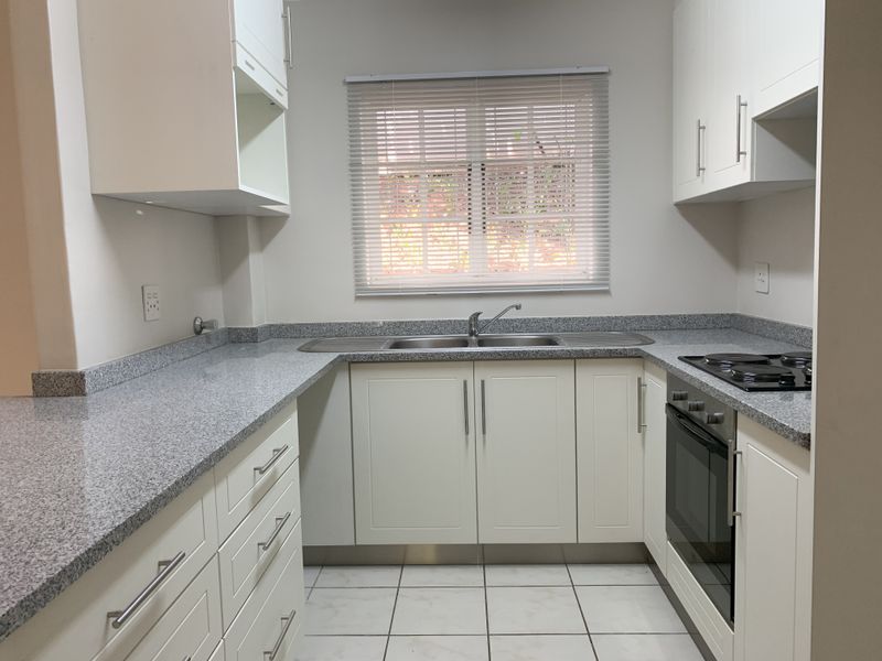 A clean, modern kitchen featuring white cabinetry, granite countertops, a built-in oven, electric hob, and a stainless steel double sink.