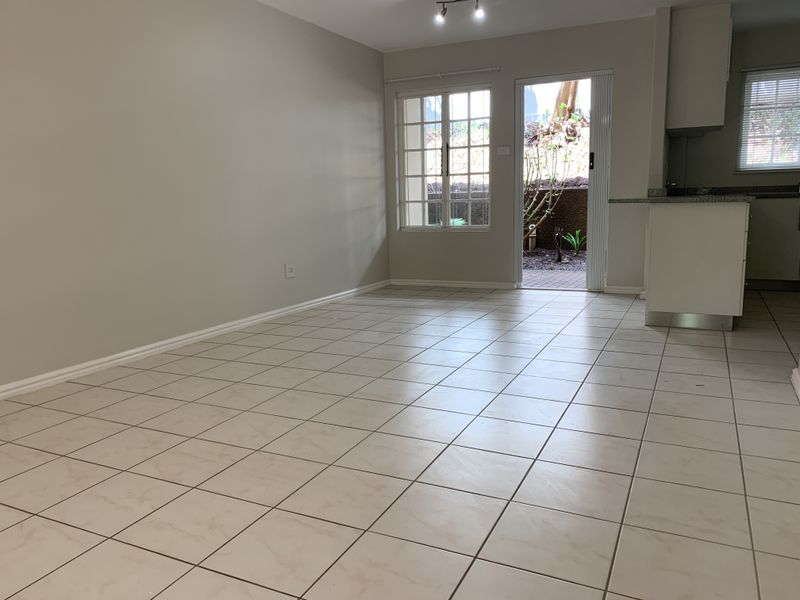 An open-plan living and kitchen area featuring neutral tiled flooring, track lighting, and direct access to an outdoor patio space.
