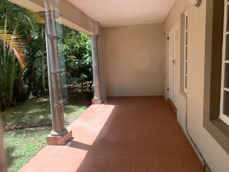 A covered patio featuring terracotta tiling, decorative columns, and glass enclosure panels, providing a seamless transition to the garden area.