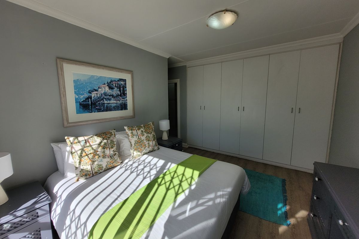A well-maintained bedroom featuring extensive built-in cupboards, laminate flooring, and neutral wall finishes.