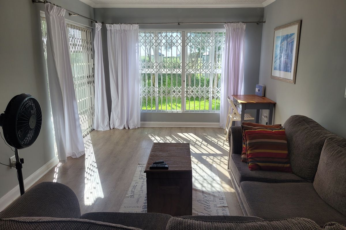 A bright living room featuring laminate flooring, security gates on windows and doors, and neutral wall tones, offering a functional and well-lit living space.