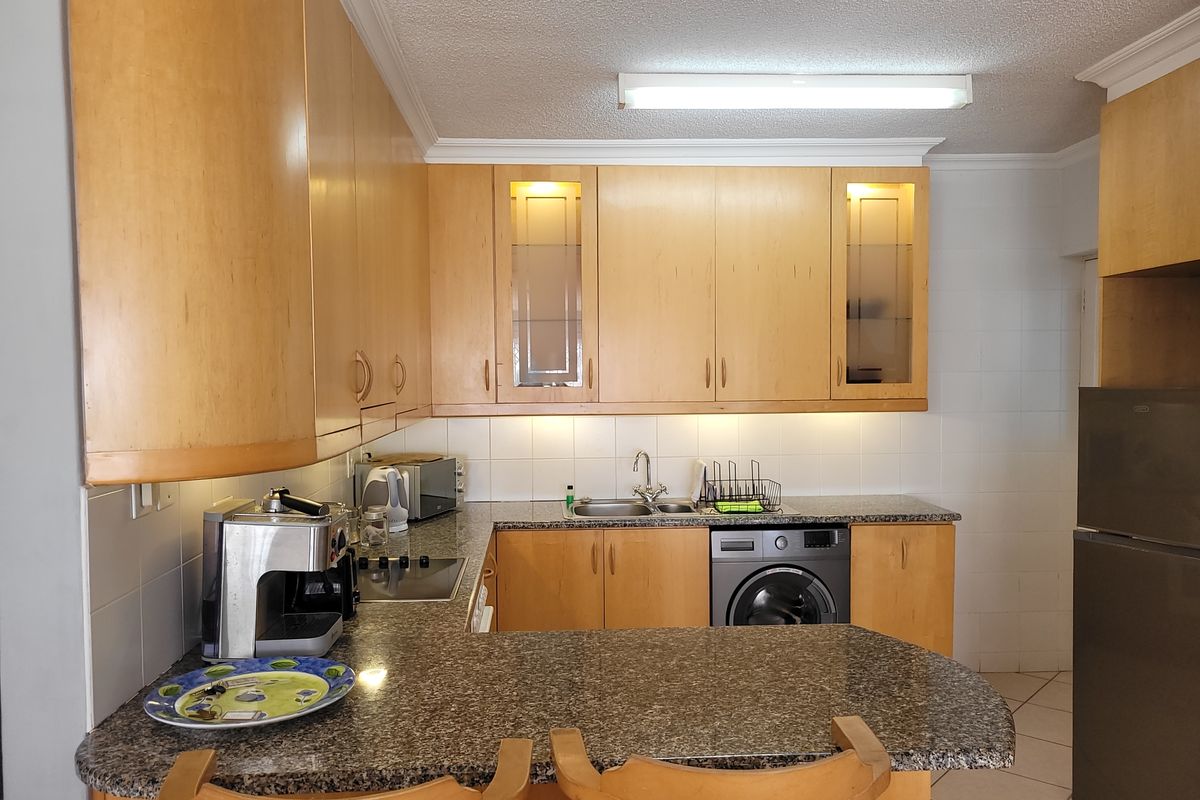 Functional kitchen featuring granite countertops, ample built-in cabinetry, integrated washing machine, and a breakfast bar, offering a practical layout for daily use.