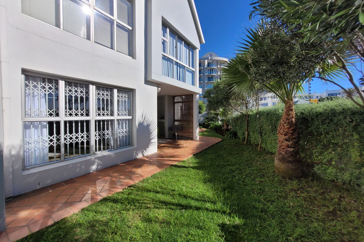 Rear view of the apartment featuring a terracotta tiled patio, well-maintained garden, and secure aluminium-framed windows.