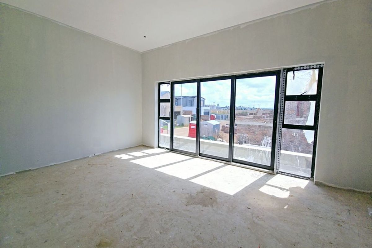 An unfinished living room space featuring large black aluminium sliding doors, currently in a shell condition awaiting final flooring and wall finishes.