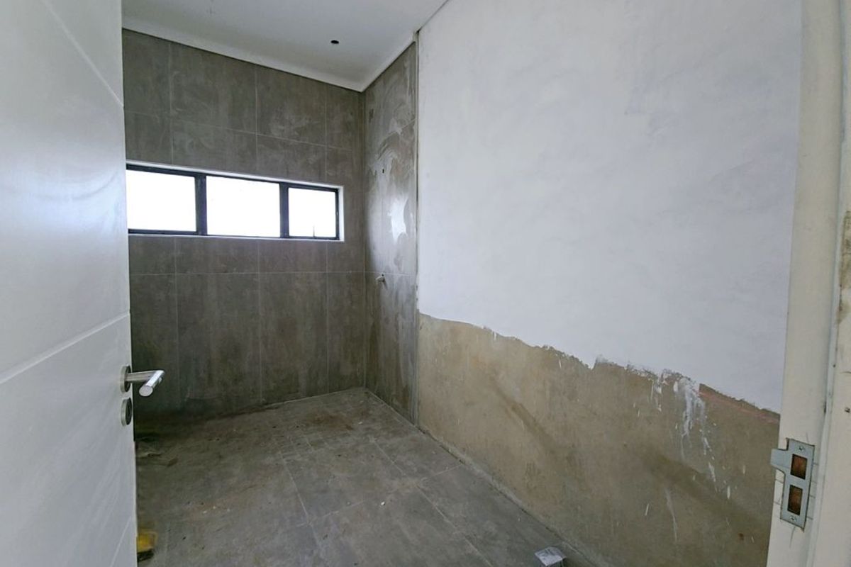 An unfinished bathroom space featuring tiled flooring and partial wall tiling, requiring final plastering, painting, and fixture installation to complete the room.