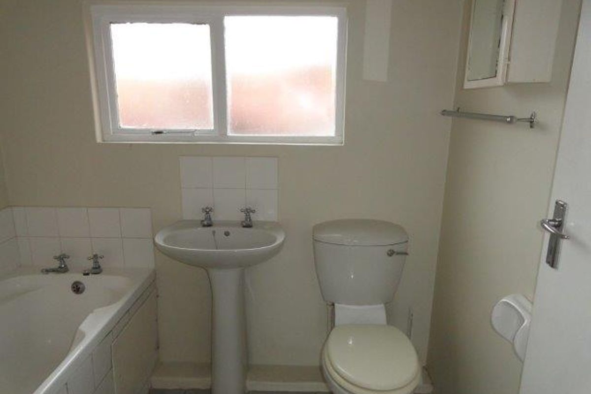 A functional bathroom featuring a pedestal basin, toilet, and bathtub with tiled splashbacks, offering a clean and simple layout.