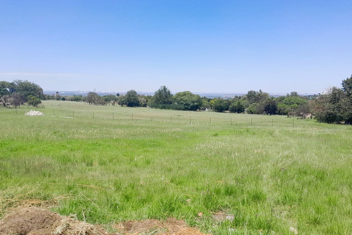 A wide-angle view of a vacant residential plot featuring open grassland and perimeter wire fencing under a clear blue sky.