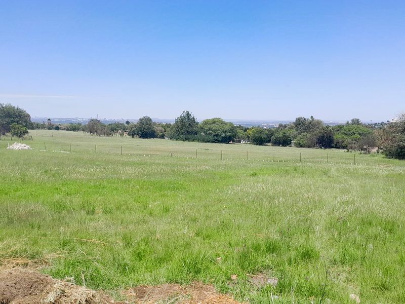 A wide-angle view of a vacant residential plot featuring open grassland and perimeter wire fencing under a clear blue sky.