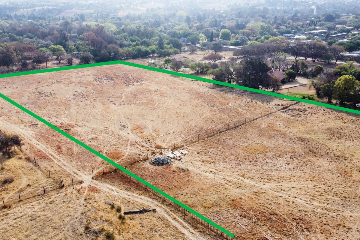 Aerial view of a vacant residential plot featuring dry grass and perimeter fencing, situated in a suburban neighborhood setting.