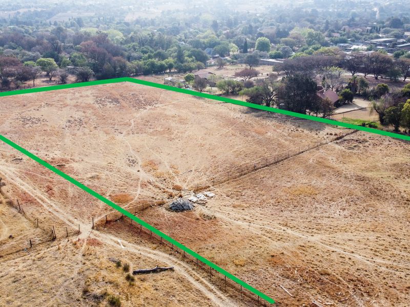 Aerial view of a vacant residential plot featuring dry grass and perimeter fencing, situated in a suburban neighborhood setting.