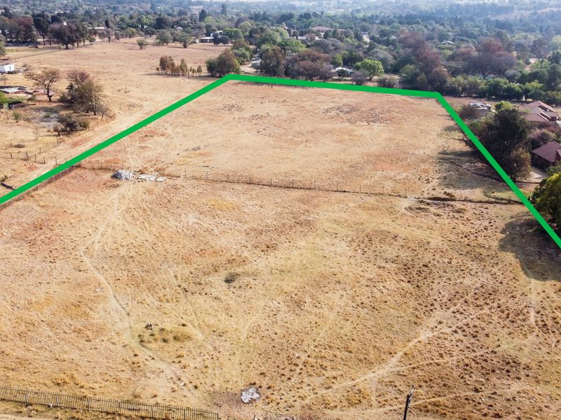 An aerial view of a large, vacant residential plot of land with perimeter fencing, situated in a semi-rural neighborhood.