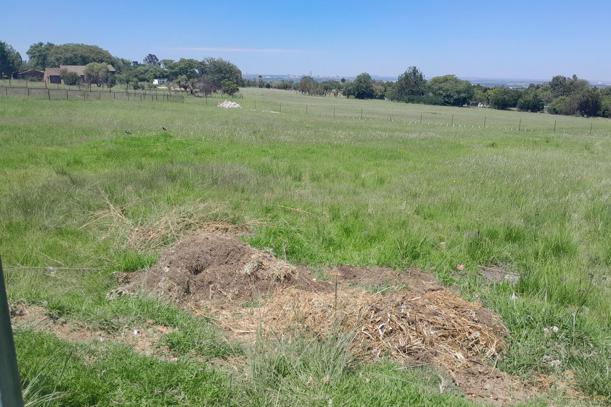 A wide, open vacant residential plot featuring natural grass coverage and perimeter wire fencing, offering expansive views of the surrounding landscape.