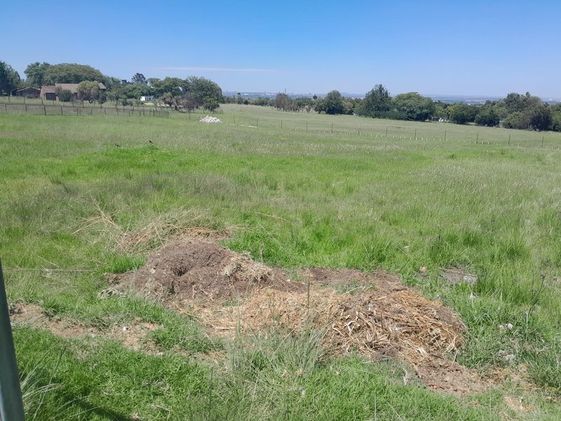 A wide, open vacant residential plot featuring natural grass coverage and perimeter wire fencing, offering expansive views of the surrounding landscape.