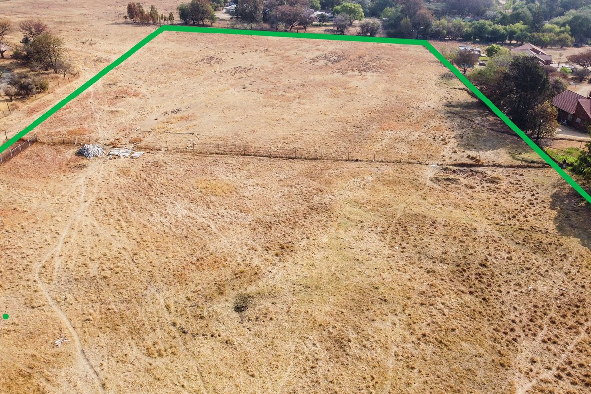 An aerial view of a vacant residential plot featuring dry grass and perimeter wire fencing, highlighting the property boundaries.