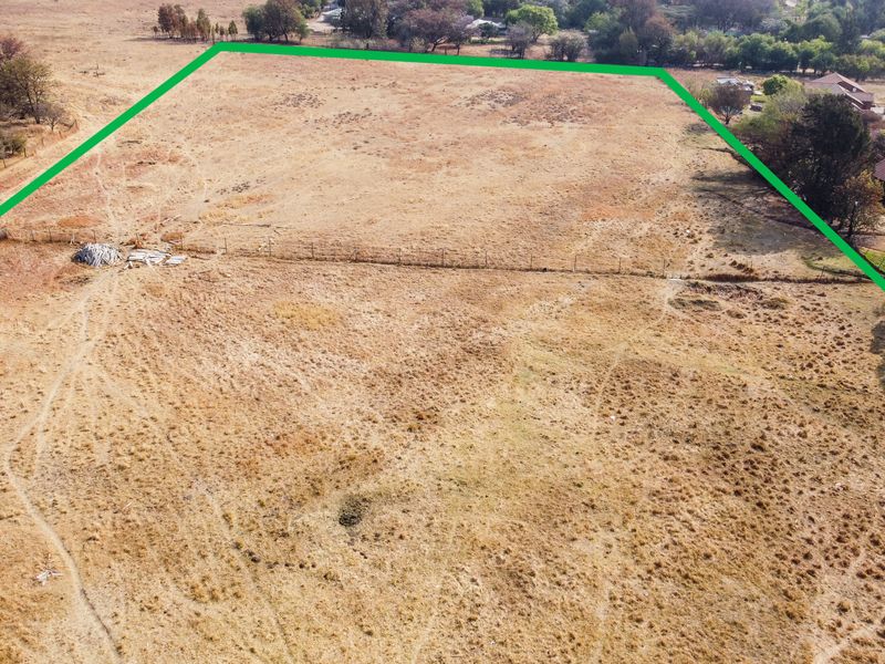 An aerial view of a vacant residential plot featuring dry grass and perimeter wire fencing, highlighting the property boundaries.