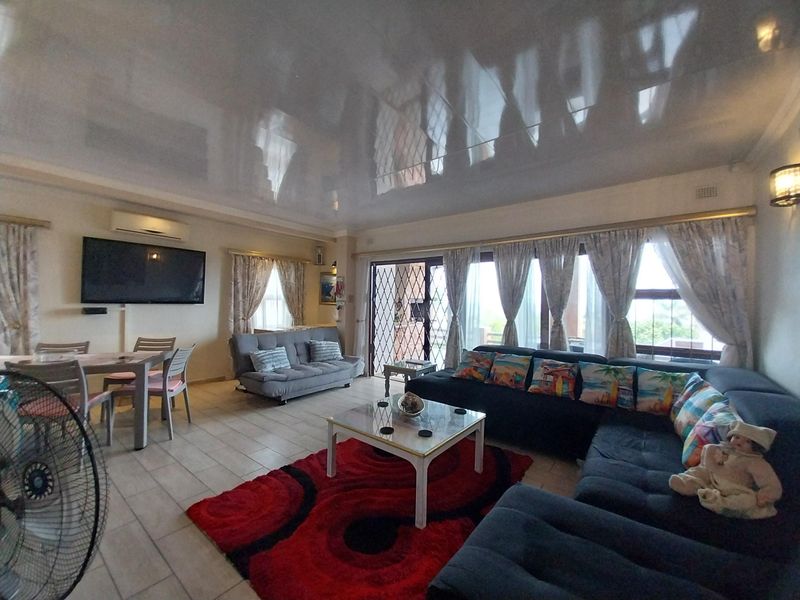 Spacious open-plan living area featuring tiled flooring, a high-gloss ceiling, wall-mounted air conditioning unit, and sliding glass doors leading to the exterior.