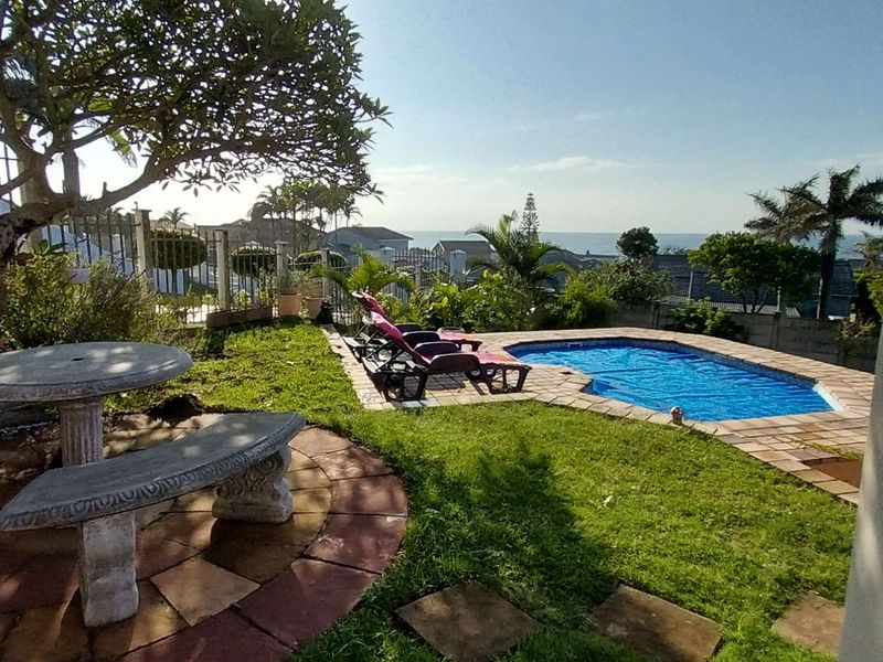 Outdoor pool area featuring a paved surround, landscaped garden, and scenic coastal views, providing a tranquil space for relaxation and outdoor enjoyment.