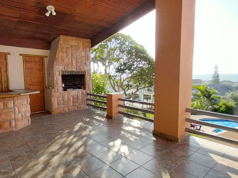 Covered patio featuring a built-in stone braai, bar area, and tiled flooring, offering elevated views of the surrounding neighborhood and distant ocean.
