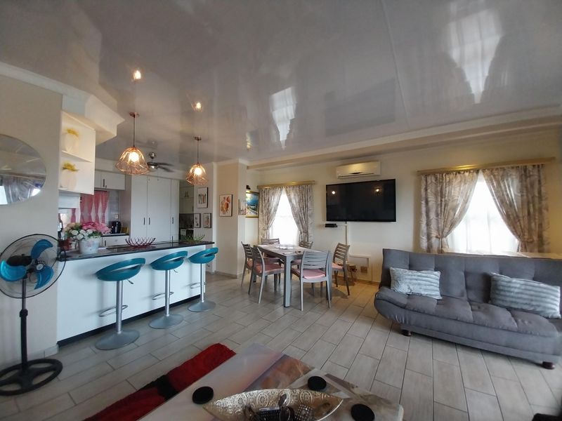 Open-plan living area featuring a kitchen with breakfast bar, dining space, and lounge area with tiled flooring and a glossy ceiling finish.