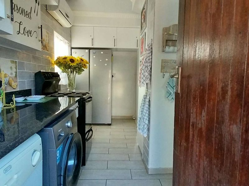 A functional kitchen featuring granite countertops, tiled flooring, built-in cabinetry, and a wall-mounted air conditioning unit.