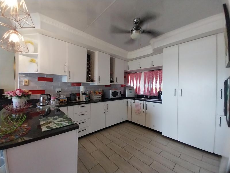 A well-maintained kitchen featuring white cabinetry, dark granite countertops, a tiled backsplash, and a ceiling fan.