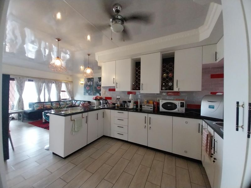 Open-plan kitchen featuring white cabinetry, dark countertops, and a breakfast bar, seamlessly flowing into the adjacent living area with tiled flooring throughout.