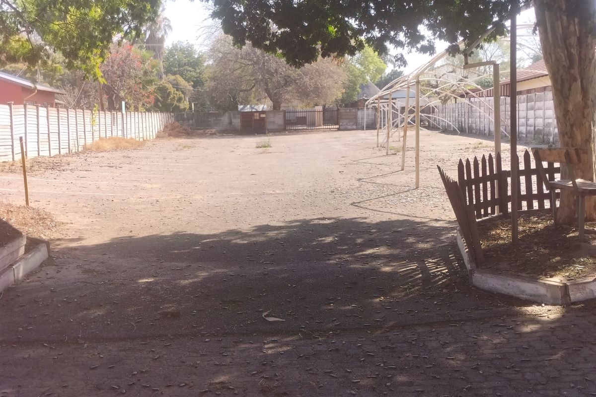 A spacious, paved rear yard area featuring a metal carport structure and secure perimeter walling, offering significant potential for landscaping or outdoor development.