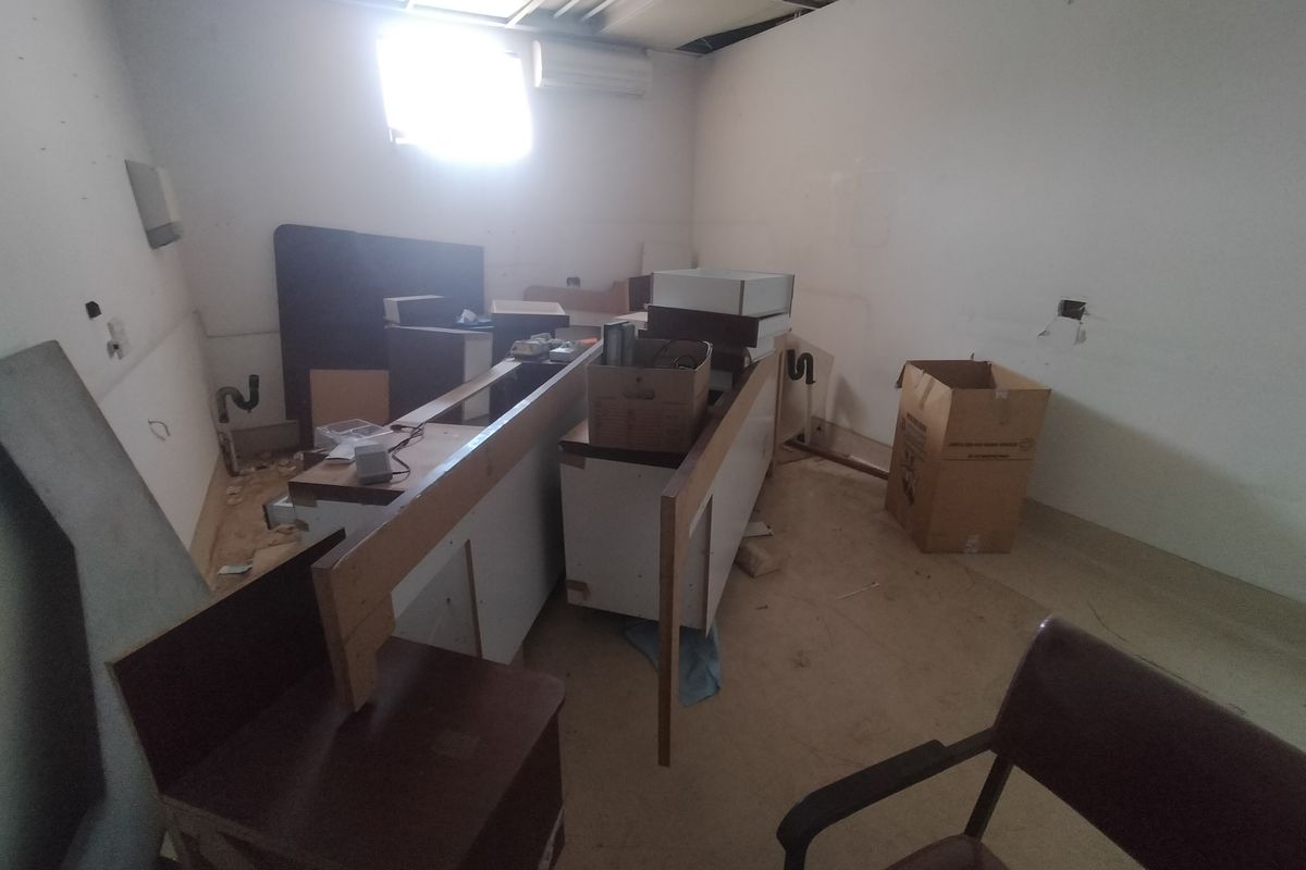 A dilapidated kitchen space requiring significant renovation, featuring exposed plumbing, missing ceiling tiles, and incomplete cabinetry installation.