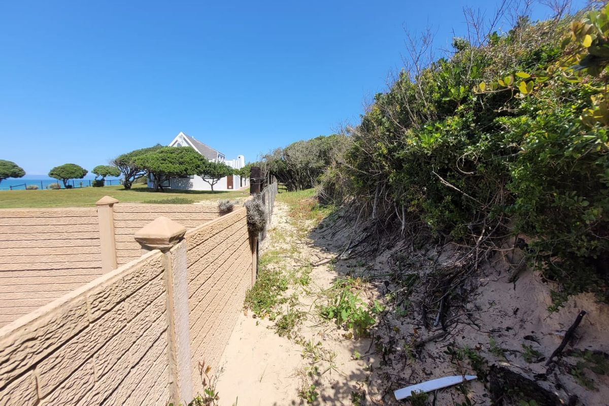 A view of the rear boundary featuring a precast concrete wall bordering a sandy area with dense coastal vegetation.