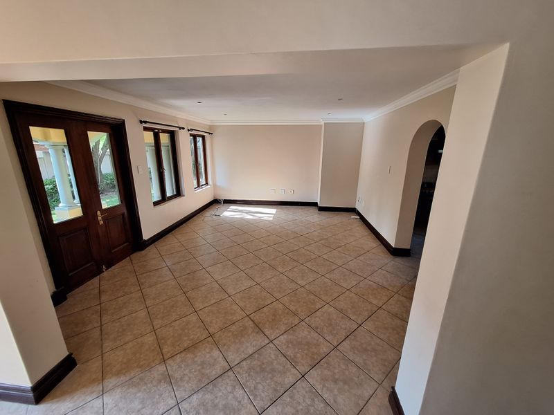 A spacious, empty living area featuring neutral tiled floors, coved cornicing, and a classic arched doorway leading to an adjacent room.