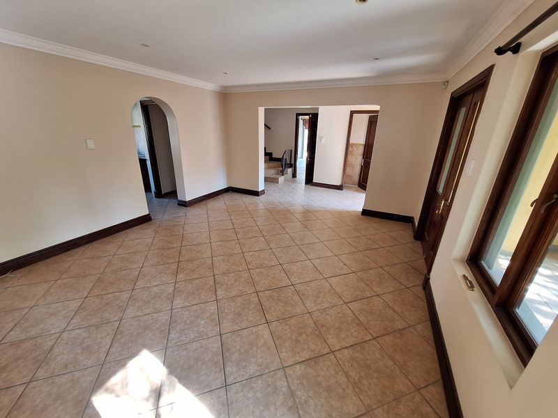 Spacious, empty living area featuring neutral walls, tiled flooring, and classic timber door frames, offering a versatile layout with access to adjoining rooms.