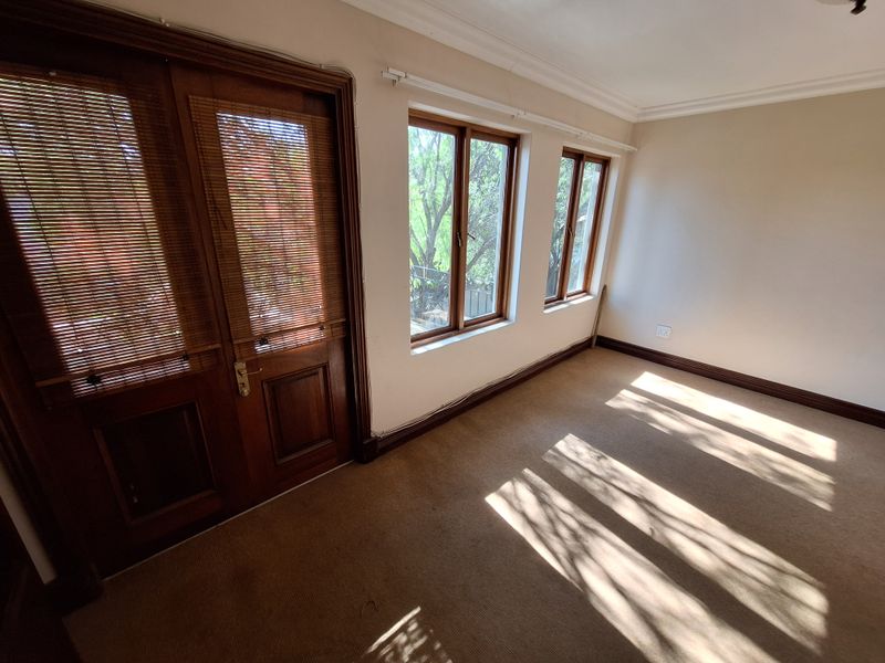 An empty living room featuring wooden double doors, timber-framed windows, and carpeted flooring, offering a neutral canvas for potential interior updates.