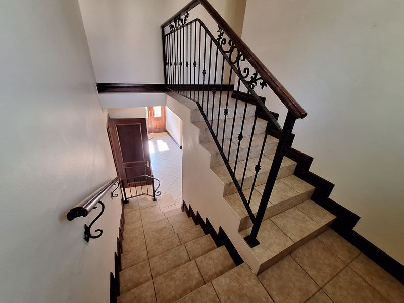 A bright entrance foyer featuring a tiled staircase with a decorative wrought iron balustrade and timber handrail, leading to the main entrance door.