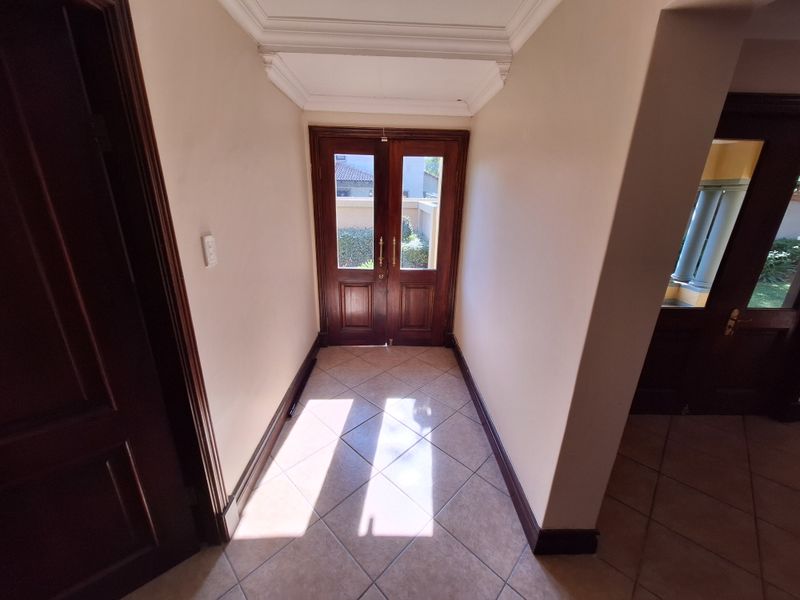 A bright and welcoming entrance hall featuring double timber doors, ceramic tiled flooring, and classic cornice detailing.