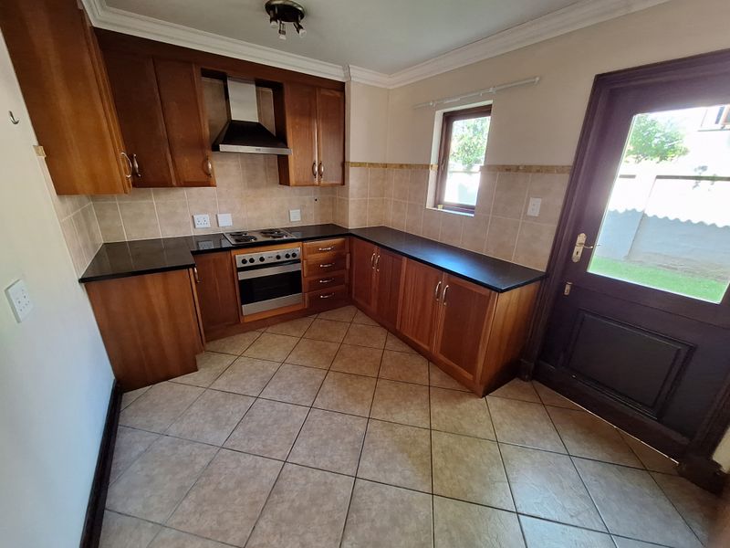 A functional kitchen featuring warm-toned wooden cabinetry, black granite countertops, tiled flooring, and integrated appliances, with direct access to the exterior.