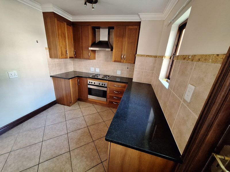 A functional kitchen featuring wooden cabinetry, granite countertops, built-in oven and hob, and tiled flooring, offering a clean and well-maintained workspace.