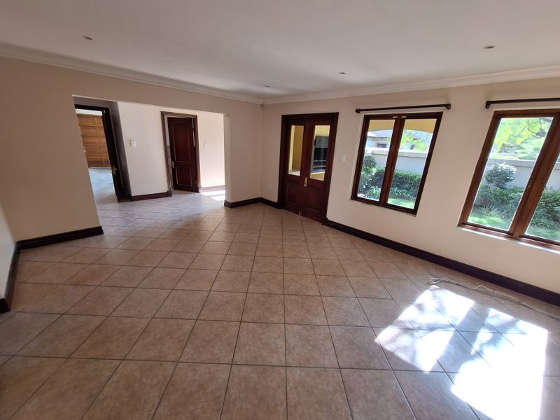 A spacious, empty living area featuring neutral walls, ceramic tiled flooring, and wooden door and window frames with natural light.